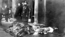 Police-officer-with-bodies-of-triangle-fire-victims-at-feet-looking-up-at-workers-poised-to-jump-from-the-upper-floors-of-the-burning-asch-building
